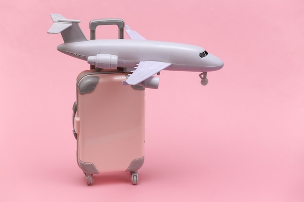 Concetto di viaggio aereo. Mini valigia da viaggio in plastica, aereo su sfondo rosa.