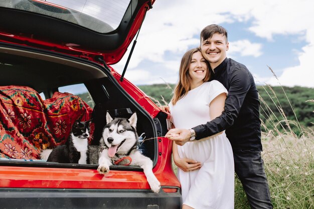 Concetto di viaggio con animali domestici L'uomo felice abbraccia la moglie incinta su uno sfondo di natura accanto all'auto