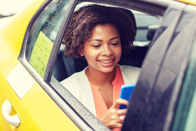concetto di viaggio d'affari, trasporti, viaggi, gesti e persone - giovane donna afroamericana sorridente che texing su smartphone in taxi in una strada della città