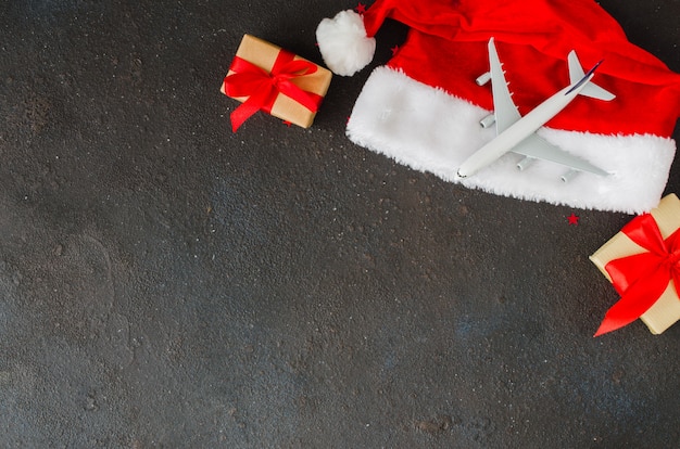 Concetto di viaggio di Natale o Capodanno. Giochi l'aeroplano sul cappello di Santa e sui contenitori di regalo su calcestruzzo scuro.