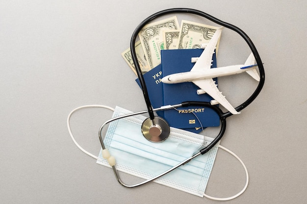 Concetto di viaggio e assistenza sanitaria. Vista dall'alto di maschera facciale, disinfettante per le mani, passaporto, stetoscopio e aereo giocattolo isolato su sfondo blu con spazio per la copia.