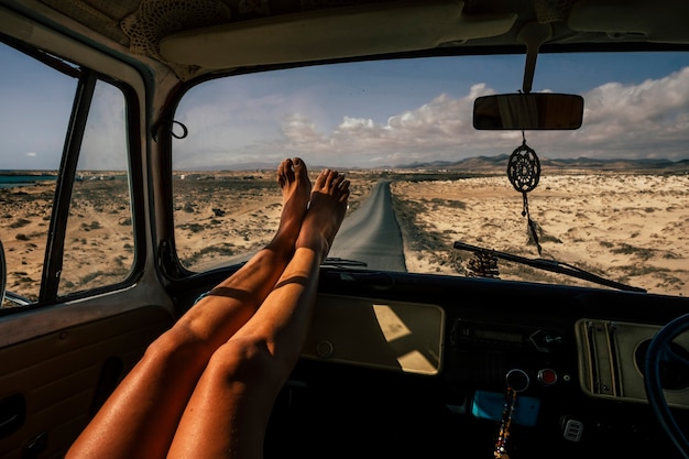 Concetto di viaggio e libertà persone con primo piano di gambe di donna godersi il viaggio su strada all'interno di un vecchio furgone vintage - ragazza stile di vita vanlife con asfalto lungo la strada sullo sfondo