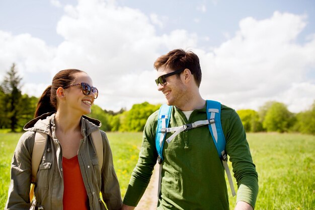 concetto di viaggio, escursionismo, zaino in spalla, turismo e persone - coppia felice con zaini che si tengono per mano e camminano lungo la strada di campagna all'aperto