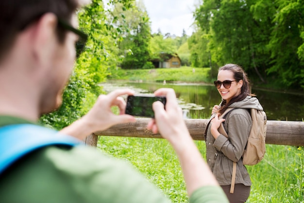 concetto di viaggio, escursionismo, zaino in spalla, turismo e persone - coppia sorridente con zaini che scattano foto con lo smartphone in natura