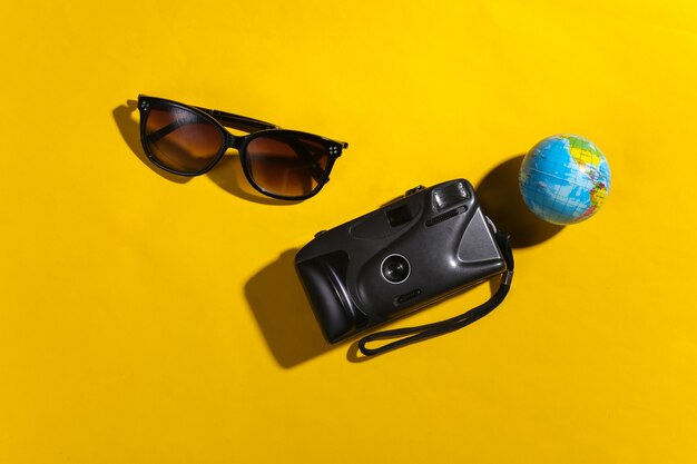 Concetto di viaggio. Fotocamera, globo, occhiali da sole su sfondo giallo con ombra. Vista dall'alto
