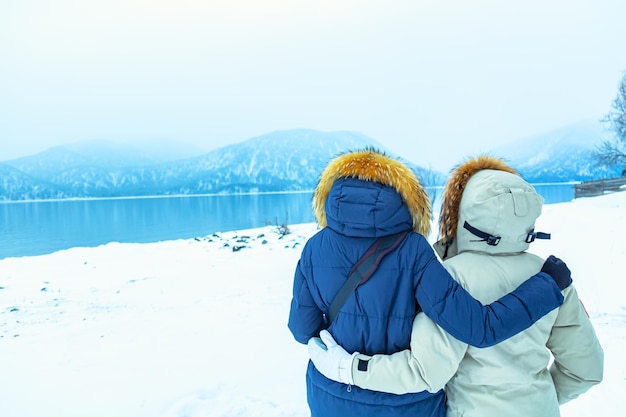 Concetto di viaggio LGBT. Abbracciate le ragazze delle escursioni in piumini in piedi vicino al lago e alle montagne in inverno.