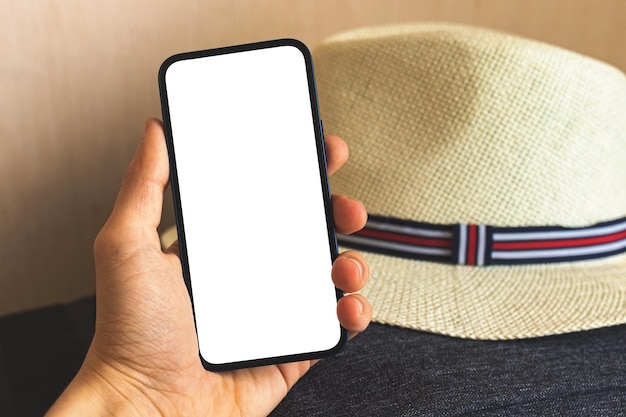 Concetto di viaggio mockup man mano tenere smartphone con schermo bianco vuoto su sfondo di cappello di paglia copia spazio foto