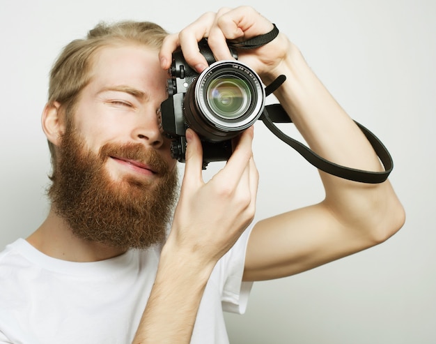 Concetto di viaggio, tecnologia e stile di vita: giovane fotografo barbuto che scatta foto con la fotocamera digitale.