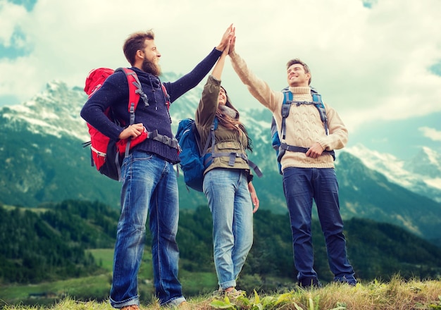 concetto di viaggio, turismo, escursione, gesto e persone - gruppo di amici sorridenti con zaini che fanno il cinque su sfondo di montagne alpine