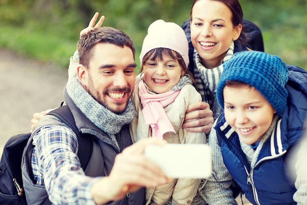 concetto di viaggio, turismo, escursione, tecnologia e persone - famiglia felice con zaini che prendono selfie con lo smartphone nei boschi