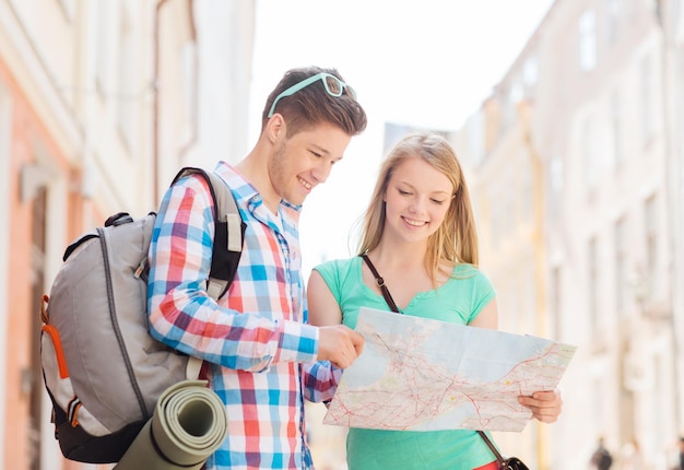 concetto di viaggio, vacanza e amicizia - coppia sorridente con mappa e zaino in città
