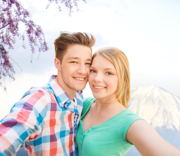 concetto di viaggio, vacanza, tecnologia, persone e amore - coppia sorridente che si fa selfie con la fotocamera o lo smartphone sullo sfondo delle montagne del Giappone