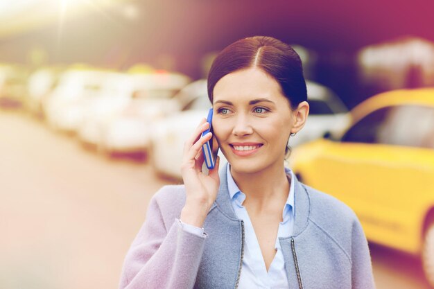 concetto di viaggio, viaggio d'affari, persone e turismo - giovane donna sorridente che chiama e parla sullo smartphone sulla stazione dei taxi o sulla strada della città