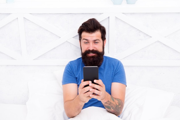 Concetto di videochiamata Comunicazione cellulare Ragazzo moderno che parla su smartphone a letto Uomo bello con moderno telefono cellulare da casa Tecnologia moderna per la vita di tutti i giorni Comunicazione moderna