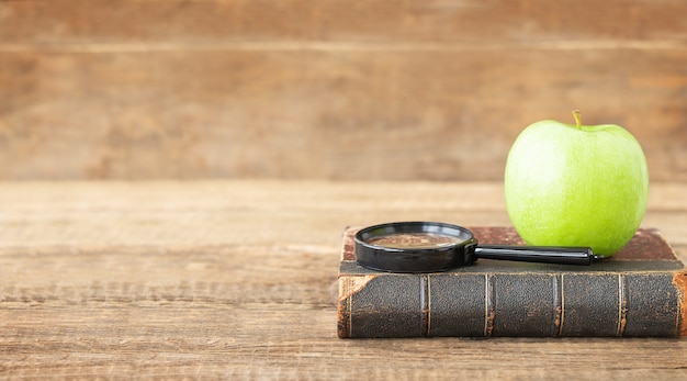 Concetto educativo Lente d'ingrandimento del vecchio libro e mela verde su uno sfondo di legno e posto per il testo