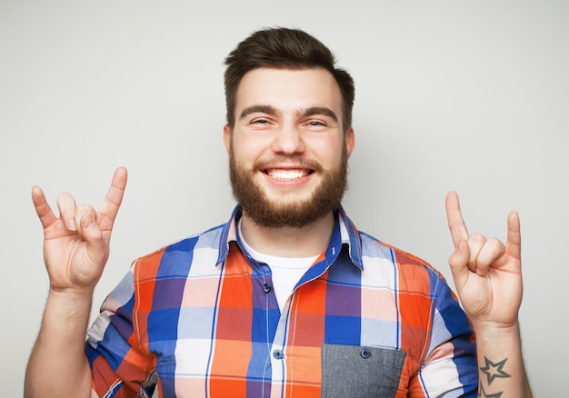 Concetto emotivo e di persone: giovane uomo barbuto che mostra un gesto pesante su sfondo grigio