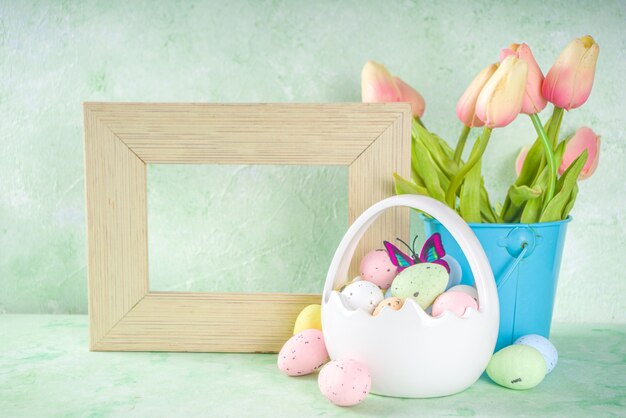 Concetto felice di Pasqua con le uova di Pasqua nel cestino e fiori primaverili. Sfondo di Pasqua con copia spazio e cornice per foto