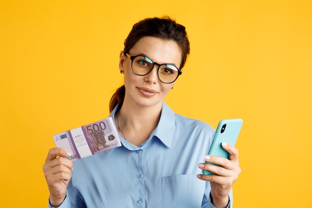 Concetto in linea di vendita. Elegante imprenditrice con soldi e telefono in studio giallo.