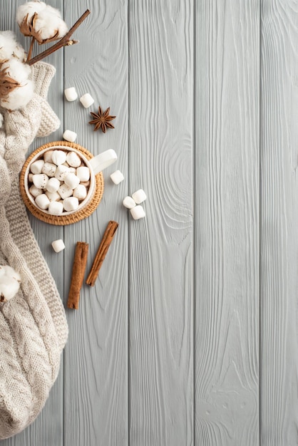 Concetto invernale Vista dall'alto foto verticale della tazza di bevanda calda con marshmallow su tovaglietta in rattan ramo di cotone accogliente sciarpa lavorata a maglia anice e bastoncini di cannella su sfondo grigio scrivania in legno