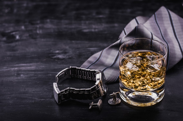 Concetto maschile per la festa del papà. Cravatta, orologi, gemelli e un bicchiere di whisky con ghiaccio