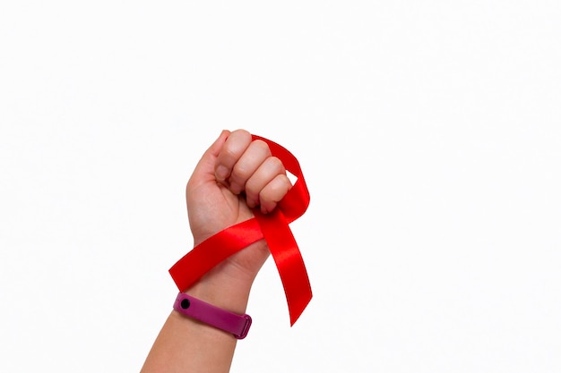 Concetto medico per la Giornata mondiale contro l'AIDS a dicembre. Nastro rosso di sensibilizzazione sull'AIDS stretto nella mano di una donna su uno sfondo bianco. copia spazio