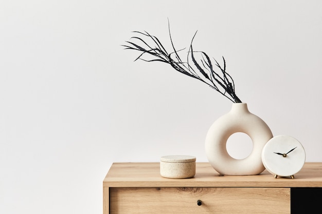 Concetto minimalista dell'interno del soggiorno in un elegante appartamento con comò in legno, foglia in vaso di ceramica, orologio ed eleganti accessori personali nell'arredamento moderno della casa. Copia spazio. Modello. .