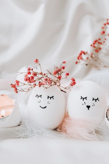 Concetto minimo di Pasqua. Uova di Pasqua con faccine sorridenti dipinte e piume di uccello su sfondo pastello. Uova di sposi. Sposato. San Valentino