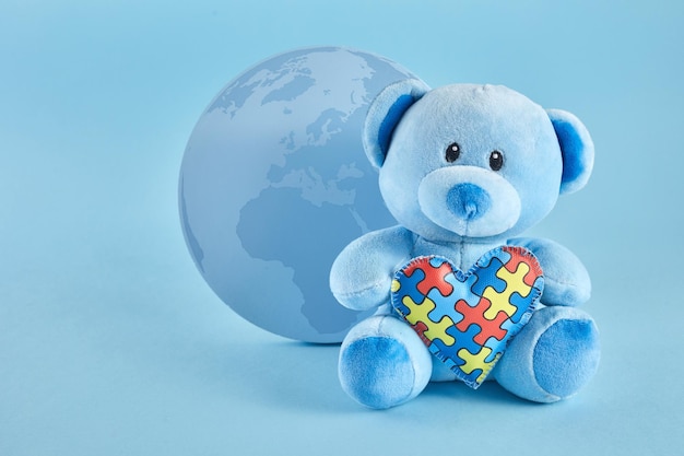 Concetto mondiale di consapevolezza dell'autismo con orsacchiotto che tiene il puzzle o il cuore del motivo del puzzle su sfondo blu