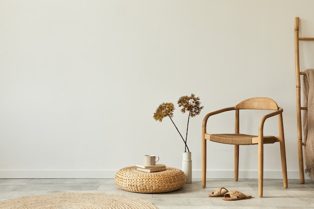 Concetto neutro dell'interno del soggiorno con sedia in legno di design, tappeto rotondo, fiori secchi in vaso, sgabello, pantofole