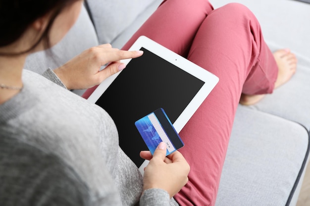 Concetto per lo shopping su Internet donna con tablet digitale e carta di credito seduta sul divano di casa