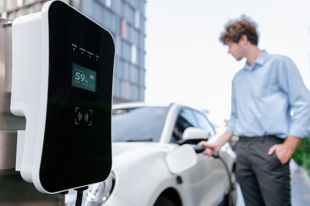 Concetto progressivo di messa a fuoco auto EV alla stazione di ricarica con sfocatura dello sfondo dell'uomo