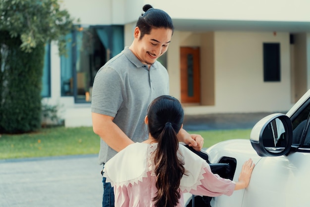 Concetto progressivo di padre e figlia con auto elettrica e stazione di ricarica domestica