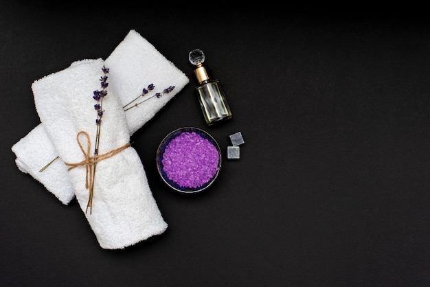 Concetto Spa. Sale di lavanda per un bagno rilassante, olio aromatico, asciugamani bianchi e fiori di lavanda secchi su sfondo nero. Aromaterapia piatto disteso.