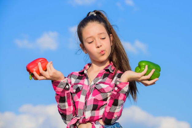 Concetto vegetariano Kid ragazza tenere peperoni rossi e verdi sullo sfondo del cielo Bambino che presenta tipi di pepe Kid tenere raccolto pepe maturo Raccolta autunnale verdure nostrane Quale pepe sceglieresti