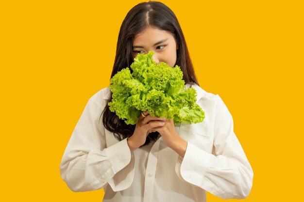 Concetto vegetariano Una donna sana in camicia bianca tiene la lattuga fresca su sfondo giallo isolato