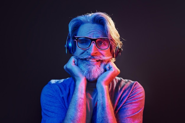 Concezione di illuminazione al neon della festa L'uomo anziano moderno ed elegante con capelli grigi e barba è al chiuso