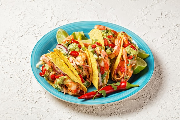 Conchiglie di taco con gamberi grigliati insalata di cavolo lime e guacamole su un piatto blu su un tavolo bianco
