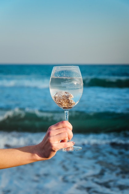 Conchiglie in un bicchiere in una mano femminile su uno sfondo di mare blu