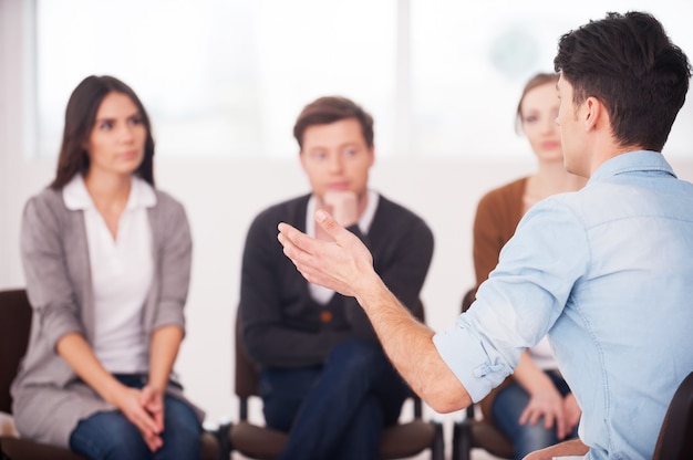 Condividere i suoi problemi con le persone. vista dell'uomo che dice qualcosa e gesticola mentre un gruppo di persone si siede di fronte a lui e ascolta