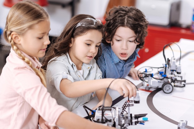 Condivisione di punti di vista. Bambini capaci e ottimisti attivi seduti a scuola e si godono le lezioni mentre esprimono interesse e discutono di progetti tecnologici