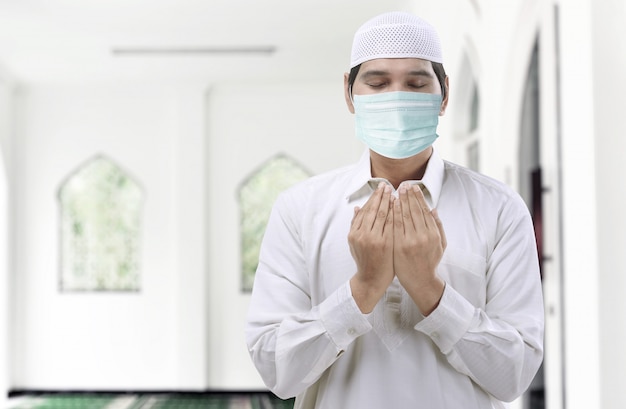 Condizione d'uso della maschera di influenza dell'uomo musulmano asiatico mentre mani e pregare sollevate