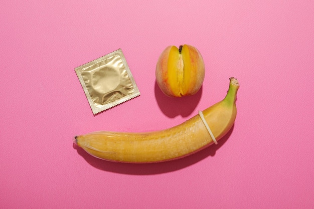 Condom su una banana con una pesca su uno sfondo rosa