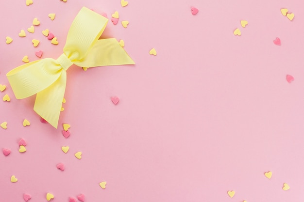 confetti a forma di cuore gialli e rosa confetti e fiocco giallo su uno sfondo rosa copia spazio