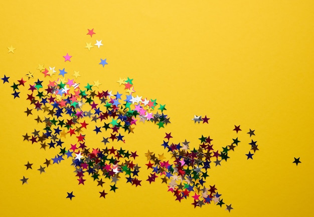 Confetti a stelle multicolori luccicanti sparsi su uno sfondo giallo sfondo festivo per il compleanno giorno di San Valentino elemento di decorazione festiva spazio di copia di design piatto
