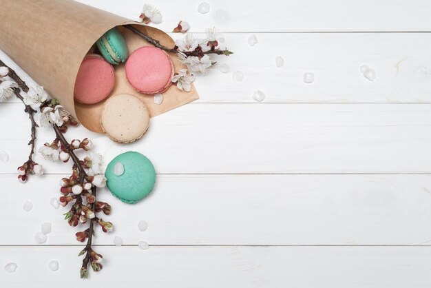 Confezione con amaretti colorati e fiori su fondo di legno bianco