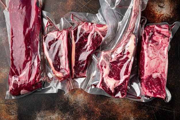 Confezione da mercato in plastica con set di bistecca di manzo fresca, tomahawk, t bone, bistecca club, rib eye e tagli di filetto, su vecchio fondo rustico scuro, vista dall'alto piatta