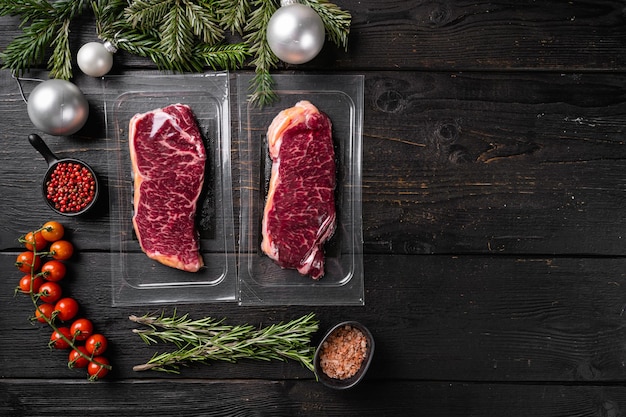 Confezione di bistecche di carne di manzo marmorizzata per il set di Natale e Capodanno, su sfondo di tavolo in legno nero, vista dall'alto piatto, con spazio per la copia del testo