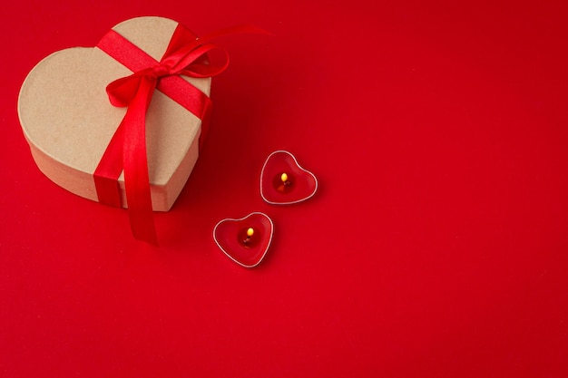 Confezione regalo a forma di cuore con fiocco e due candele su sfondo rosso San Valentino