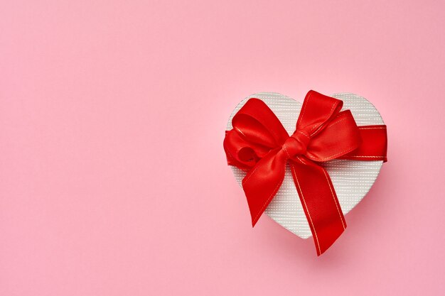 Confezione regalo a forma di cuore con un nastro rosso su sfondo rosa. Cartolina di concetto di San Valentino. Vista dall'alto.