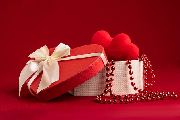 Confezione regalo a forma di cuore su fondo rosso con cuori e perline all'interno di un bellissimo set di...